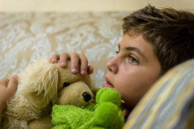 Boy with stuffed toy looking away on sofa at home