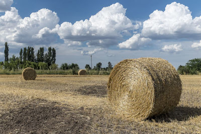 Hay bales on agricultural landscape against sky