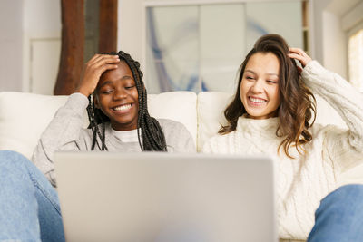Smiling lesbian women using laptop on sofa at home