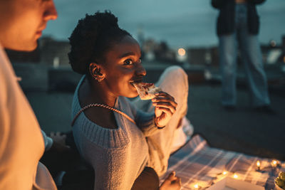 Side view of young woman drinking water while sitting on table