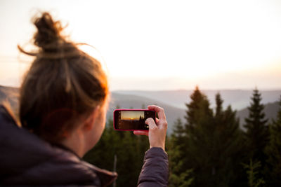 Rear view of woman photographing mountain during sunrise