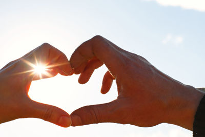 Cropped hands making heart shape against sky