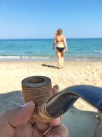 Close-up of hand holding smoking pipe with woman in background at beach