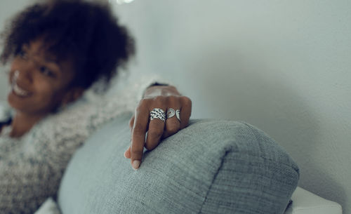 Selective focus on the hand with rings of a smiling black woman sitting on a couch