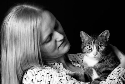 Portrait of woman with cat against black background
