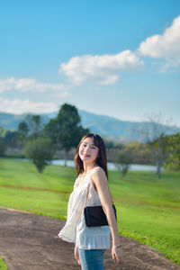 Young woman standing on field against sky