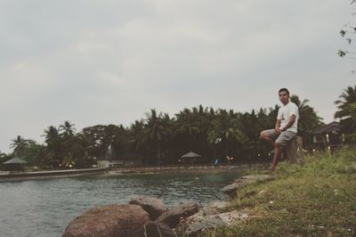 Side view of young man standing by trees against sky