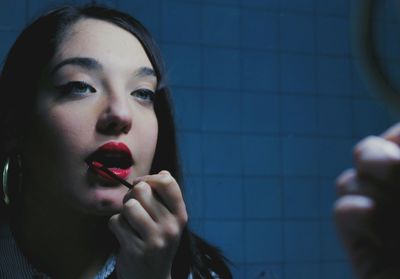 Reflection of young woman applying lipstick in mirror