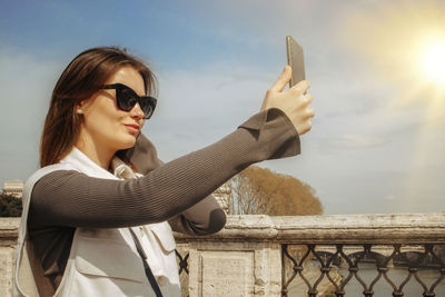 Cheerful beautiful young woman takes a selfie on a smartphone while walking in rome 