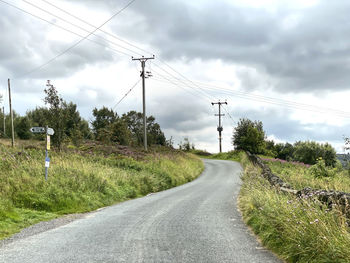 Road by electricity pylon against sky