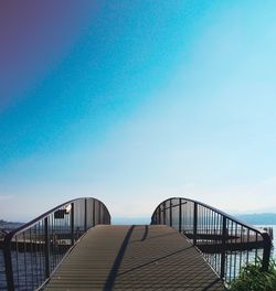 Footbridge over sea against clear blue sky