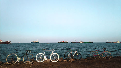 Bicycles parked at beach with ships in sea against sky