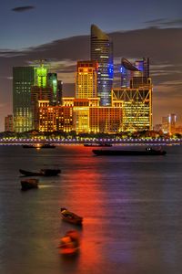 Illuminated city by river against sky at night
