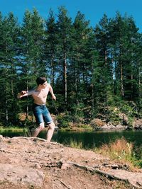 Shirtless young man skimming stones in lake a forest