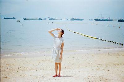 Full length of woman shielding eyes at beach