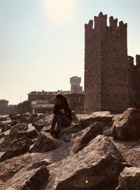 Woman sitting by historic building on rock