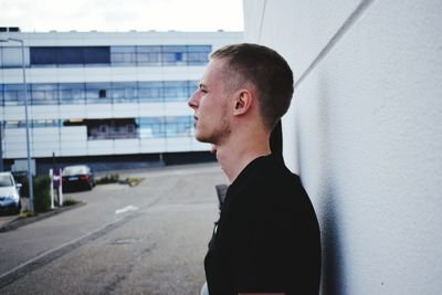 Side view of young man standing against white wall