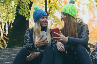 Two girls sitting in the park using smartphone. teen using mobile phone. sisters chat with friends.