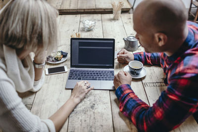 Multi-ethnic couple using laptop at table in coffee shop