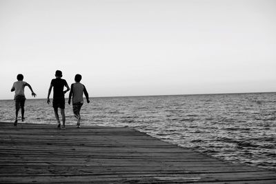 People standing on jetty by sea against clear sky