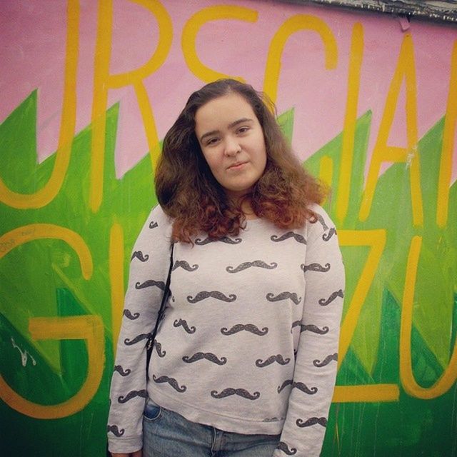 young adult, young women, person, long hair, portrait, lifestyles, looking at camera, casual clothing, front view, standing, leisure activity, three quarter length, waist up, smiling, happiness, wall - building feature, graffiti