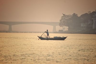 Silhouette man on boat sailing in river against sky