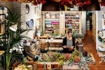 From above professional female florist arranging christmas flower bouquet while working in shop on wooden table