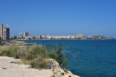 Scenic view of sea by buildings against clear blue sky