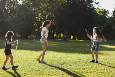 Portrait of three girls-sisters playing and blowing soap bubbles in the park.