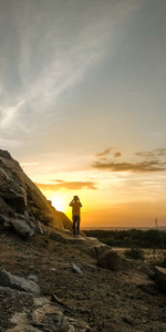 Silhouette man standing on rock against sky during sunset