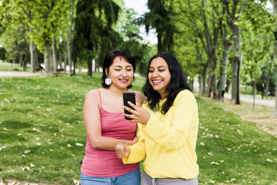 Happy young woman using phone while standing on tree