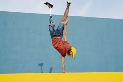 Young man with artificial limb and foot doing handstand against multi colored wall