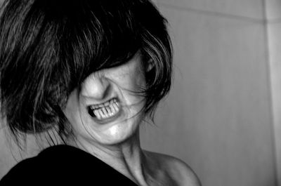 Close-up of spooky woman clenching teeth while standing against wall