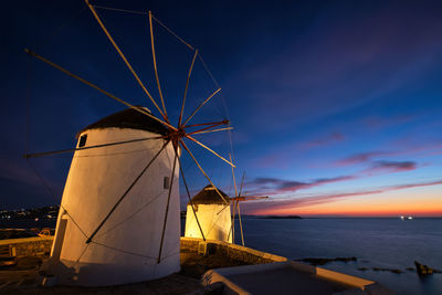 Traditional windmill by sea against sky during sunset