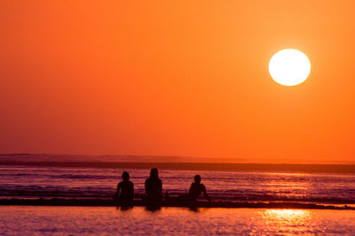 Silhouette people on beach against orange sky