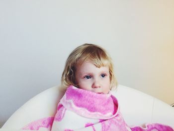 Cute girl wrapped in towel sitting on chair against wall at home