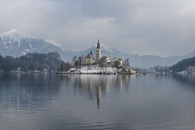 Scenic view of historic building by lake against snowcapped mountains