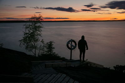 Rear view of silhouette woman standing by lake during sunset