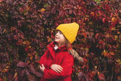 Beautiful girl in a yellow hat with her eyes closed stands against the background of autumn foliage.