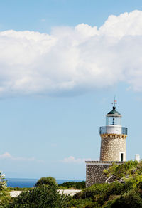 Lighthouse amidst buildings and sea against sky