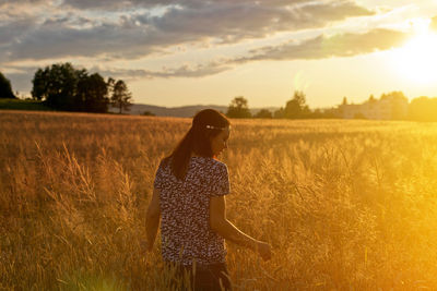 Woman standing on field against sky during sunset