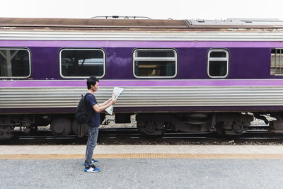 Man reading map while standing by train at railroad station