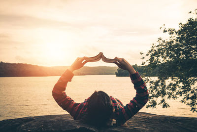 Rear view of woman in heart shape against sky during sunset