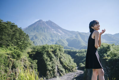 Smiling young woman standing on land against mountains and sky