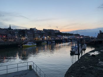 Sailboats moored in river against buildings in city at sunset