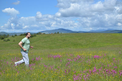 Man running in nature on a cloudy day in springtime, with hill and clouds in background