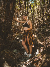Portrait of young woman standing by tree in forest