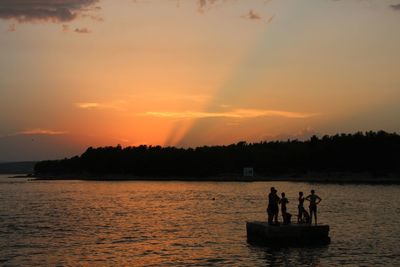 Silhouette people standing on sea against sky during sunset