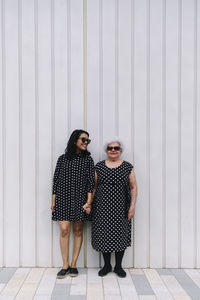 Smiling daughter with mother wearing matching outfits standing in front of white wall