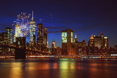 Illuminated buildings by river against sky in city at night